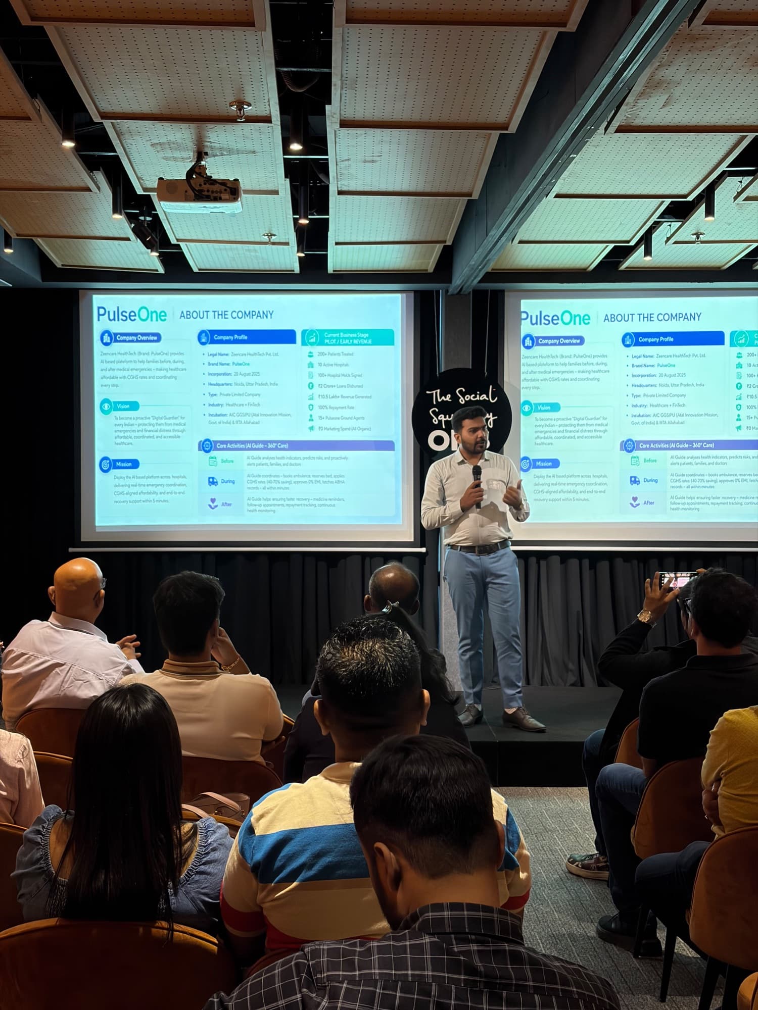 A founder presenting their startup on stage, slides behind him, to a seated audience.