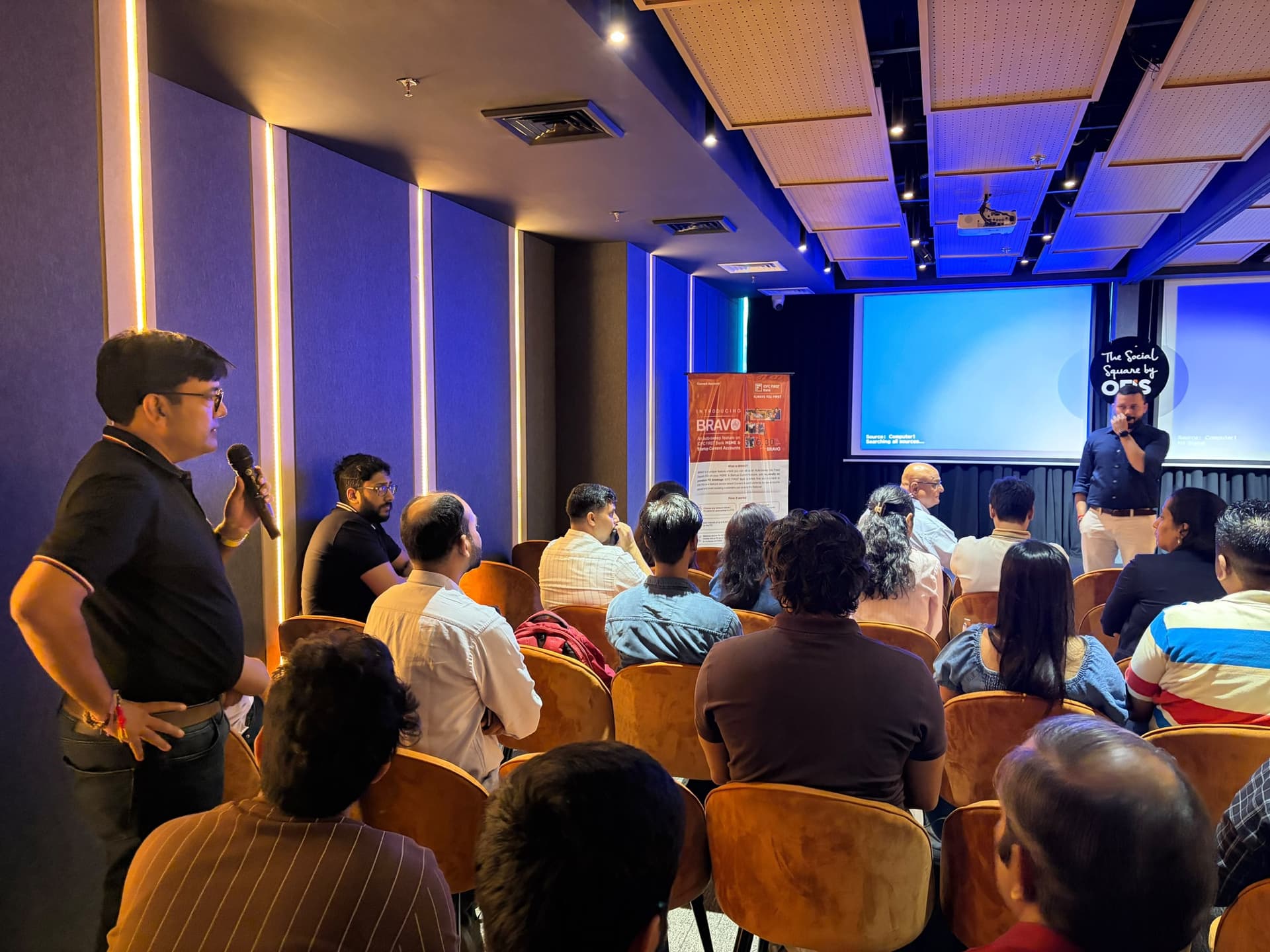 A founder in the audience asking a question with the microphone, the speaker answering from the front of the room.